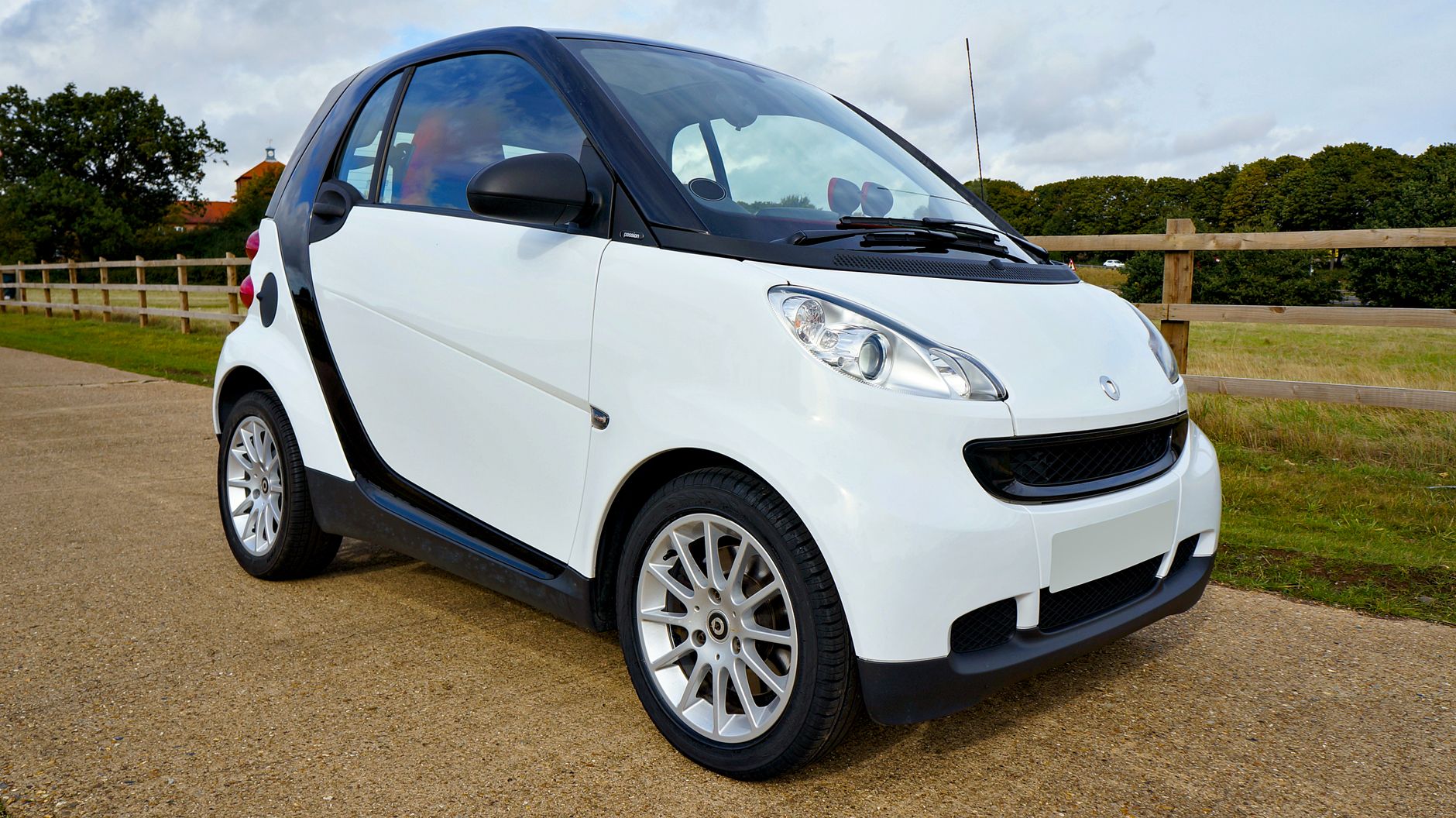 Białe micro auto Smart Fortwo zaparkowane na tle zieleni i błękitnego nieba
