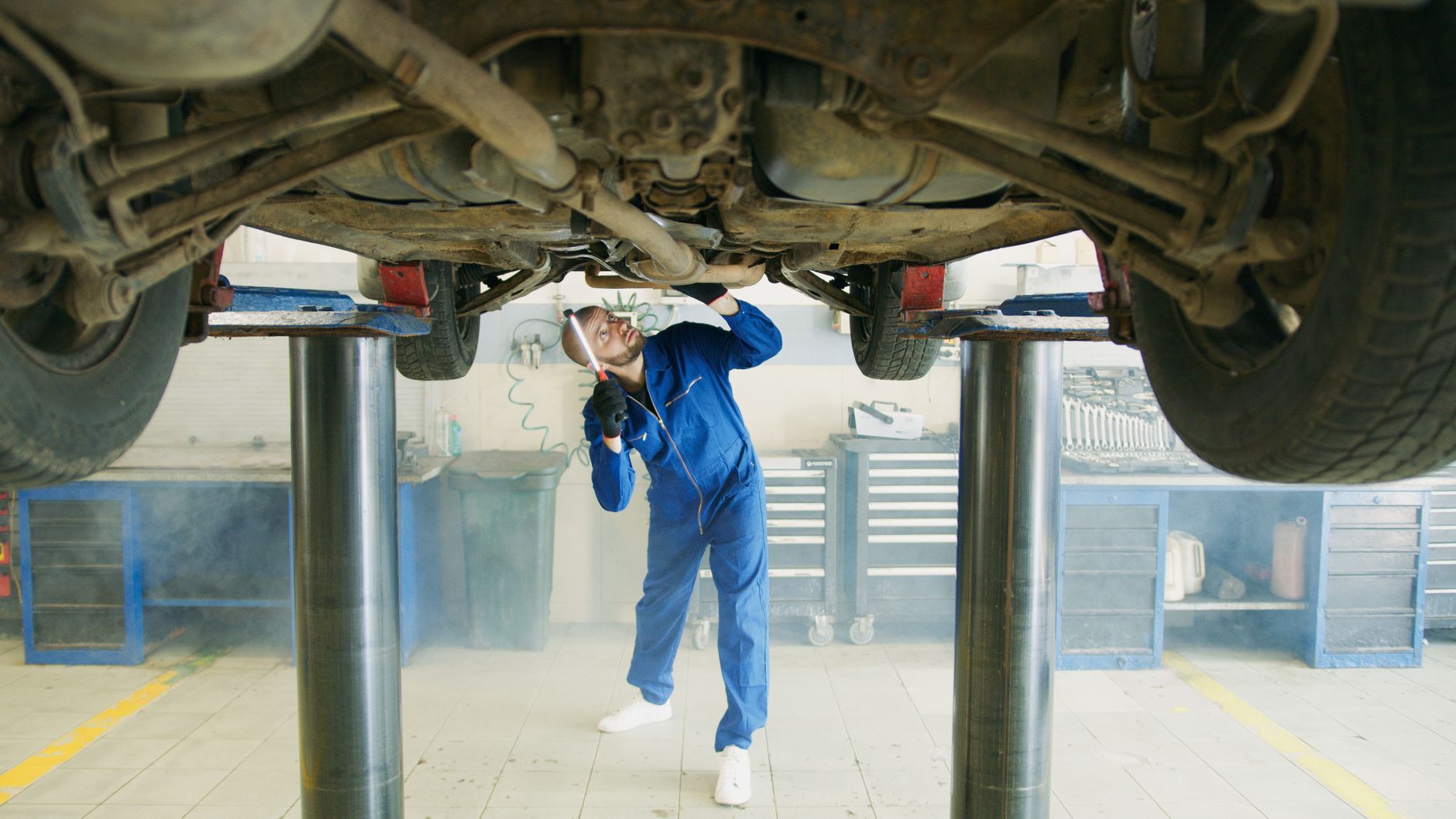 Mechanik w niebieskim kombinezonie ogląda podwozie auta na podnośniku